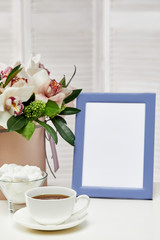 photo frame, orchid flowers, cup of tea and sweets. empty space for text. mock up with copy space.