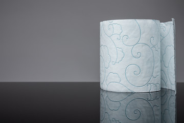 Single roll of white toilet paper on the black table, grey wall on the background