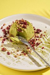 Matcha green tea, mint, lemon raw mousse cake on white plate and sunny yellow background. Contemporary minimalistic style. Raw Healthy Paleo green Avocado Cake. Tropical leaves and hard shadows around