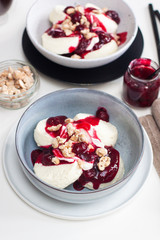 Cottage cheese pancakes with cherry sauce, sour cream and caramelized nuts on white table.