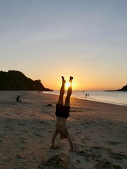 Man making handstand before sunset with orange sky at Nacpan beach, El Nido, Palawan, Philippines