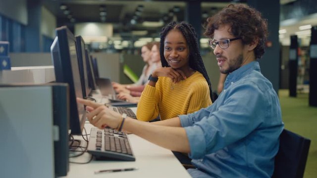 University Library: Bright Black Girl and Smart Hispanic Boy Together Work on Computers, Chat, Discuss Class Assignment, Explain and Advice Each Other. Diverse Group of Students Study Together