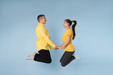 Fototapeta na wymiar Young happy couple in yellow shirts holding hands together jumping and looking at each other