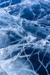 Natural texture of clear blue ice with deep cracks. Beautiful cracks in the clear ice of the lake. Vertical.
