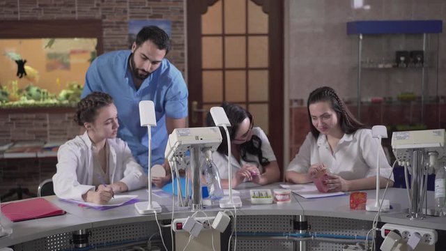 Young Caucasian woman writing notes after Middle Eastern lecturer in dental audience. Students learning stomatology, professional dentist explaining material. Education, studying, medicine.