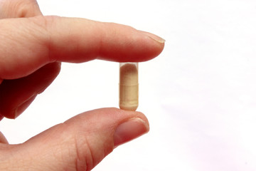 Hand holding a pill between thumb and forefinger isolated on white background