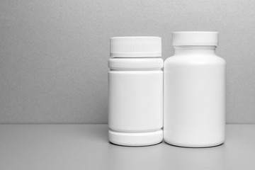 2 white jars for medicines and vitamins and dietary supplements without a name are on a gray shelf. copy space to the left. layout for a pharmacy, a store