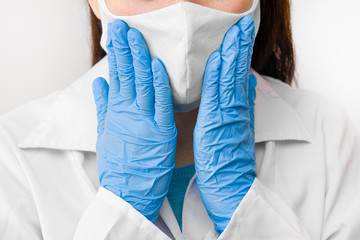 Closeup womans hands to the face in protective mask against coronavirus, SARS-CoV-2, 2019-nCoV or flu. Doctor in white labcoat, blue gloves and mask.