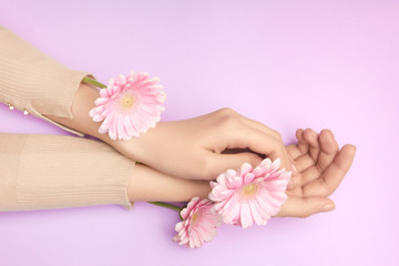 Obraz na płótnie Canvas Pink petals of a flower in gentle womans hands on a violet background. Concept of advertisment of beauty salon. A thin wrist and natural manicure.