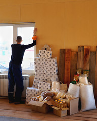 A young man looking out the window during the Covid-19 quarantine , with a mask in his hand. Stock of long- stored food and toilet paper. Panic. Self-isolation. Covid-19 Epidemic.