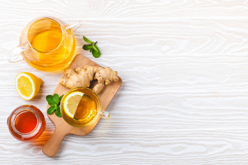 Overhead of glass cup with ginger and lemon tea, teapot, white wooden background with copy space....