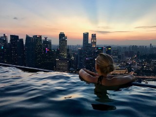 Blond woman in rooftop pool on skyscraper, with skyline in background, Singapore, South East Asia