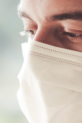 Vertical photo of a young bearded white man with a medical face mask during coronavirus quarantine. The front part of the face lightly blurred. Coronavirus, COVID-19 outbreak. Doctor, nurse concept
