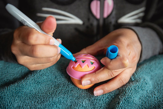 Closeup image of a child decorating an easter egg with a marker and plastic template.