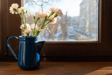 a bouquet of pink Bush carnations in a blue jug on the windowsill