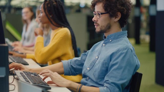 University Library: Handsome Bright Boy using Computer for Class Assignment. Diverse Multi-Ethnic Group of Students Learning, Studying for Exams, Work on Computers, Talk in College Study Room