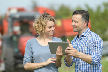 Couple of Farmer analyses the harvesting data next to the tractor in a field