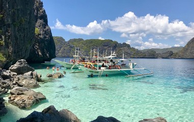 Outrigger boats at stony beach, with green and blue water, with islands in background, El Nido, Palawan, Philippines