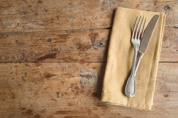 Vintage fork and knife on linen napkin on old wooden background. Space for text, top view