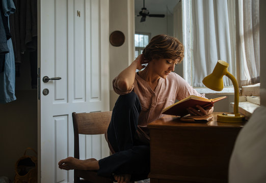 Young woman reading interesting book at table at home