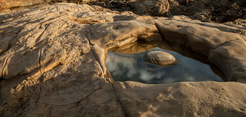 a rock sits in a reflective pool along the California coast