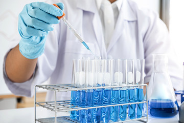 Biochemistry laboratory research, Scientist or medical in lab coat holding test tube with using reagent with drop of color liquid over glass equipment working at the laboratory