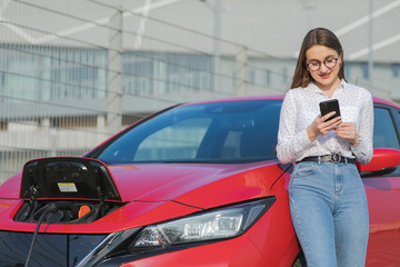 Ecological car connected and charging batteries. Girl using smartphone and waiting power supply connect to electric vehicles for charging the battery in car