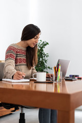 Young freelancer working from a makeshift home office connected to the internet with a laptop and a phone during the period of global confinement