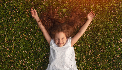 Cheerful little girl lying on green grass