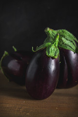 Three small purple eggplants on wood table with dark background