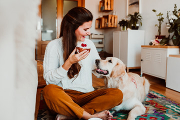 Young woman having a healthy breakfast sitting on the floor at home while she is in quarentine during the covid19 crisis accompanied by her golden retriever. Lifestyle. Stay Home