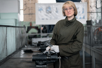 Woman factory worker is measuring a metal workpiece by a caliper.