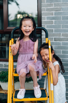 Two cute little gils laughing on a ladder, at a backyard