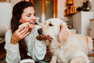 Young woman having a healthy breakfast lying on the floor at home while she is in quarentine during the covid19 crisis accompanied by her golden retriever. Lifestyle. Stay home