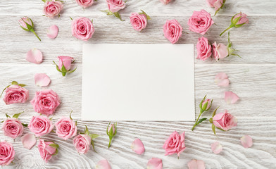 Fototapeta na wymiar Blank sheet paper with rose flowers on white wooden background with copy space for design, text. Top view of pink roses and rosebuds.