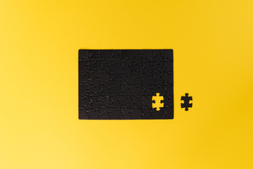 An unfinished black puzzle on a yellow background. The puzzle without one piece. Almost complete. Unfinished work concept