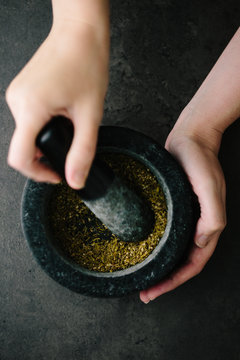 Woman gringing spice mix in a dark mortar with pestle