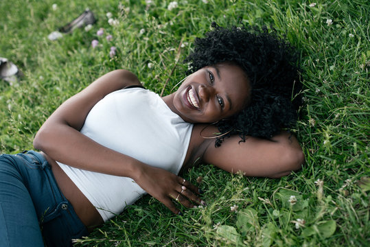 Smiling african girl is laying on the grass in jeans and white crop top.