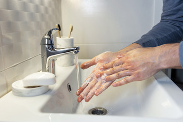 Hygiene concept. Washing hands with soap under the tap with water. Male hands and water in the bathroom.