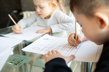 Schoolboy and schoolgirl writing letters. Close-up  pencil in the hand of child. Children learning to write letters at the table. A home distance learning.