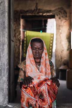 Elder woman sitting in the entrance of the house. Her face has an expression of concern
