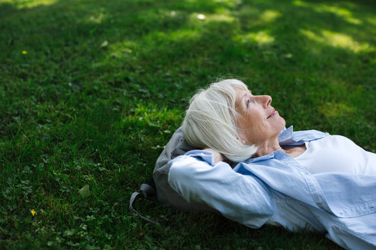 Mature woman lying in the green grass looking up.