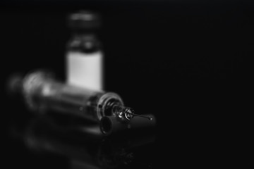 Close up of medical vial for injection with a syringe and ampoule on black background