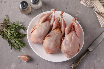 Three fresh organic quails on a white plate on a gray background, Top view