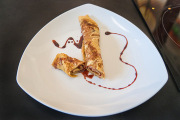 Gefüllter Crepe Pfannkuchen eingerollt und dekoriert auf weißem Teller