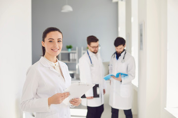 Fototapeta premium A male doctor with a stethoscope smiling a clipboard while standing in a clinic.