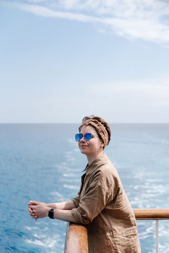 Pretty brunette leaning on rails of deck and smiling.