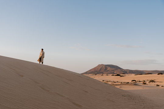 Stylish girl in coat going up on high sandy hill.