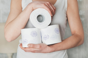 Woman holds some rolls of toilet paper in her arms in the bathroom