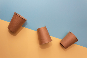 Three craft paper cups for coffee or any drinks on a blue and yellow paper background. Concept of ziro waste, no plastic